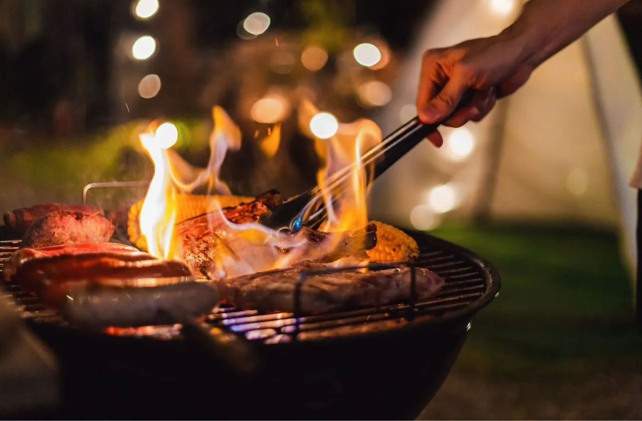 Grillades sur un barbecue au charbon, flammes et guirlandes lumineuses en soirée
