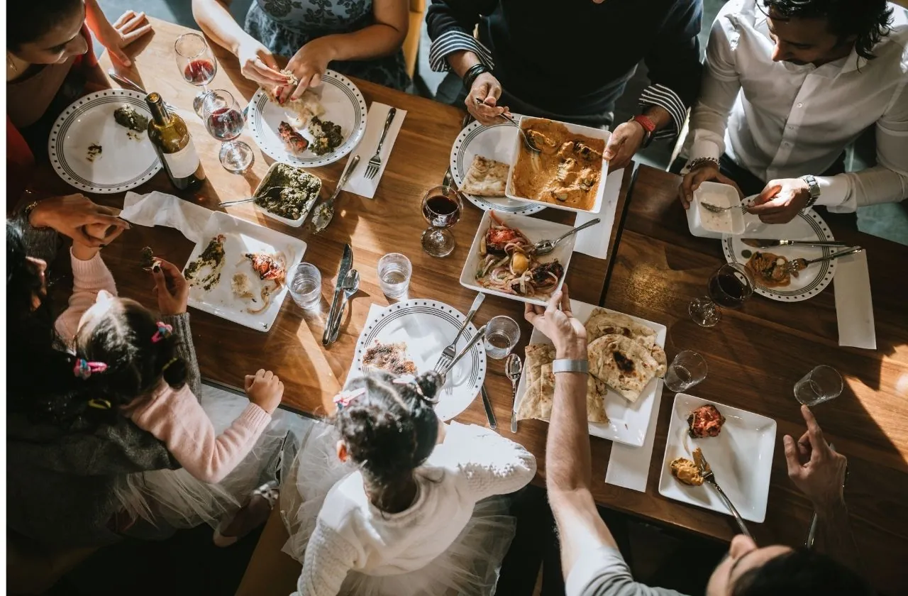 Vue en plongée d'une tablée familiale, adultes et enfants se servant de plats partagés